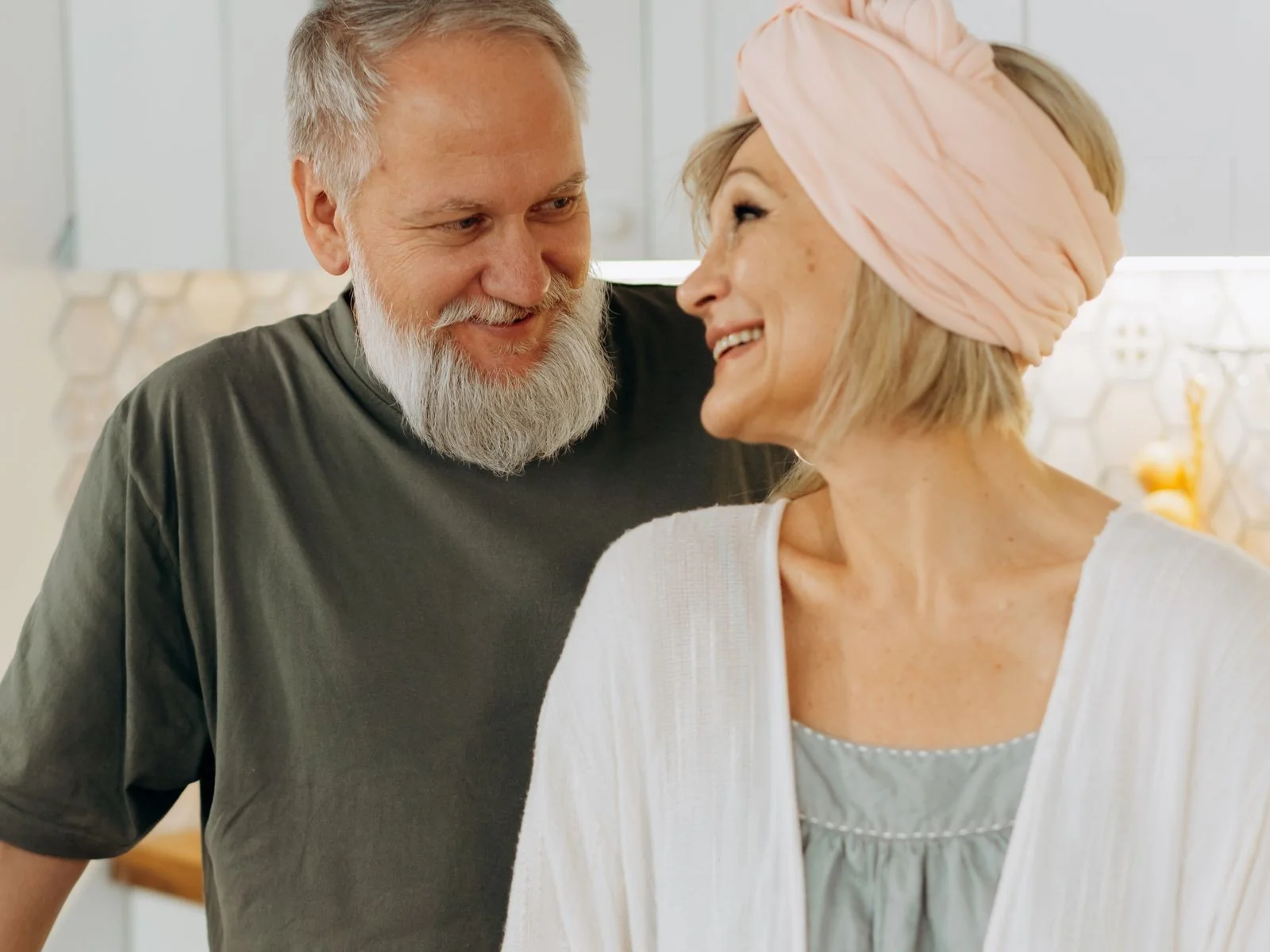 A mature couple stands close together and smiles in a bright kitchen while planning their next step.